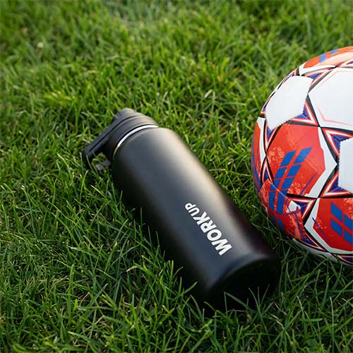 Fodbold og WORK UP-drikkeflaske ligger i græsset.