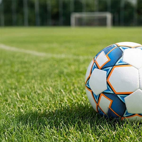 Fodbold ligger i forgrunden på en fodboldbane.