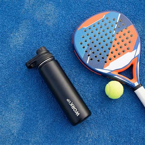WORK UP-drikkeflaske ligger på jorden ved siden af en padelketcher og en bold. 