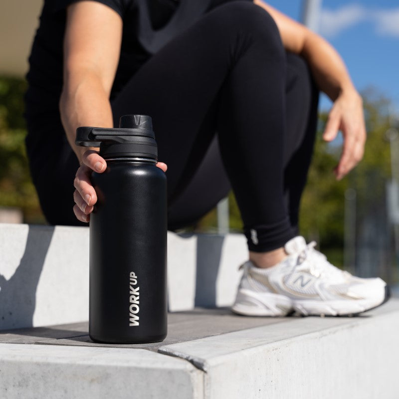 Kvinde sidder på trappe i sportstøj og holder en drikkeflaske fra WORK UP.